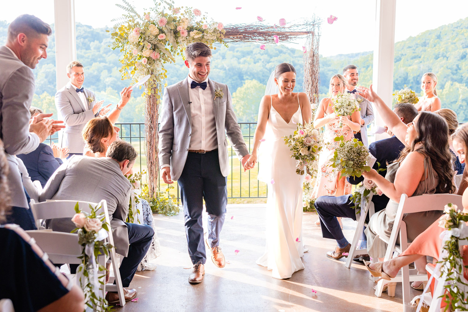 Wedding couple walking down aisle with floral arch after ceremony and guests celebrating in Cortland